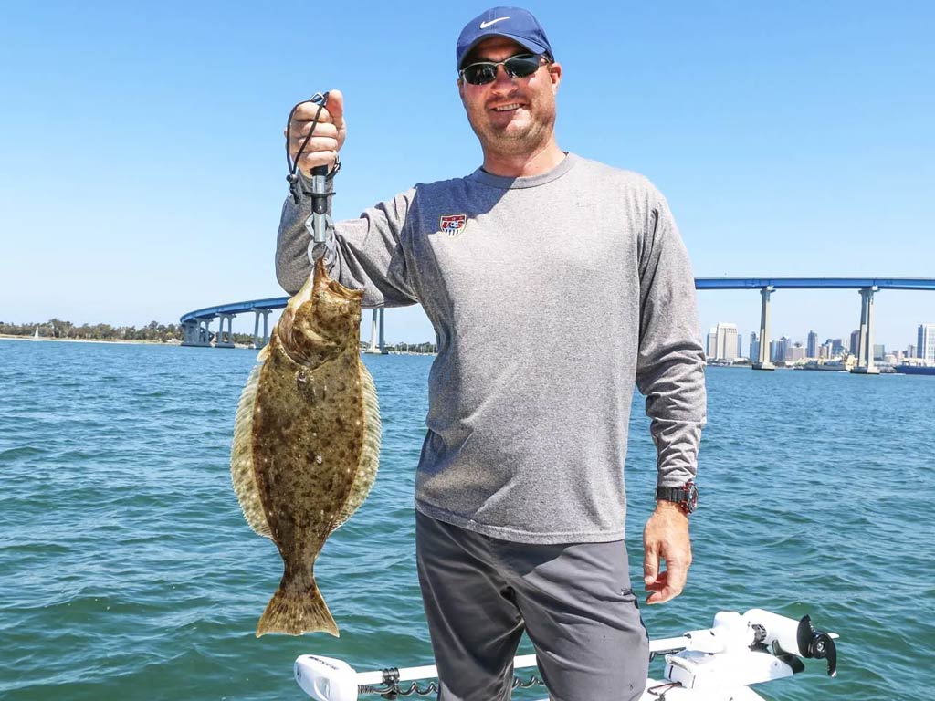 A photo featuring an angler holding a small California Halibut aboard a charter fishing vessel.