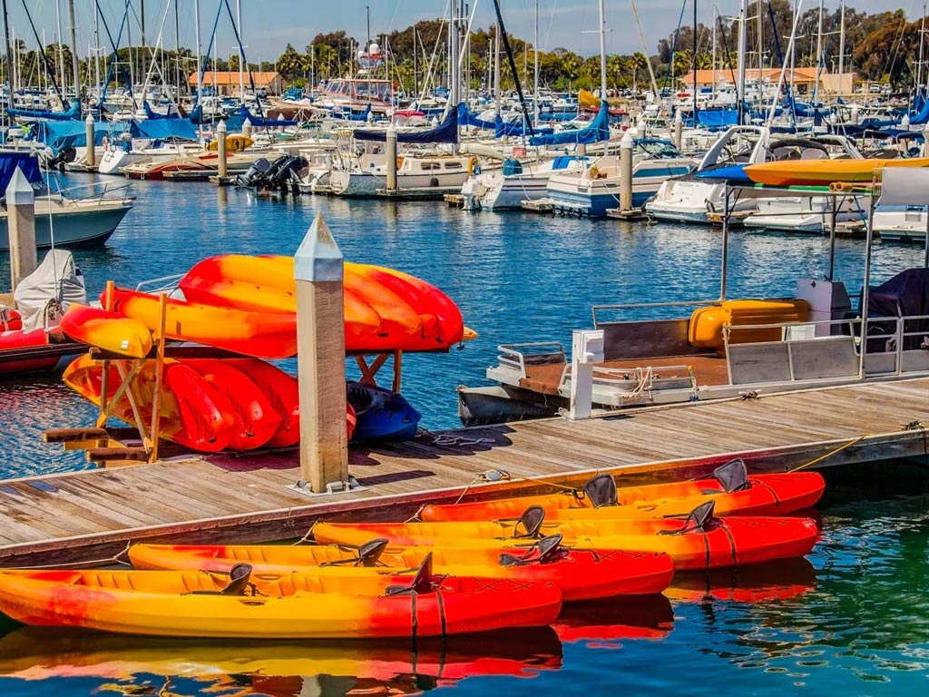 A photo featuring several orange rental kayaks tethered at Oceanside Harbor.