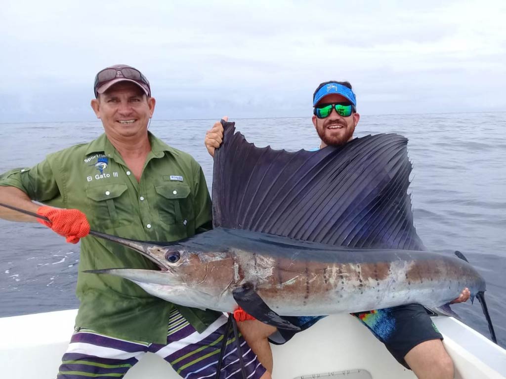 A photo of two anglers sitting on a charter fishing boat and holding big Sailfish caught during their angling trip in Boca Raton offshore fisheries