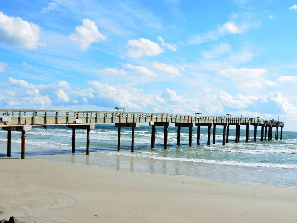 A view from the street of a beach and one of St. Augustine's fishing piers, stretching over the water on a sunny day