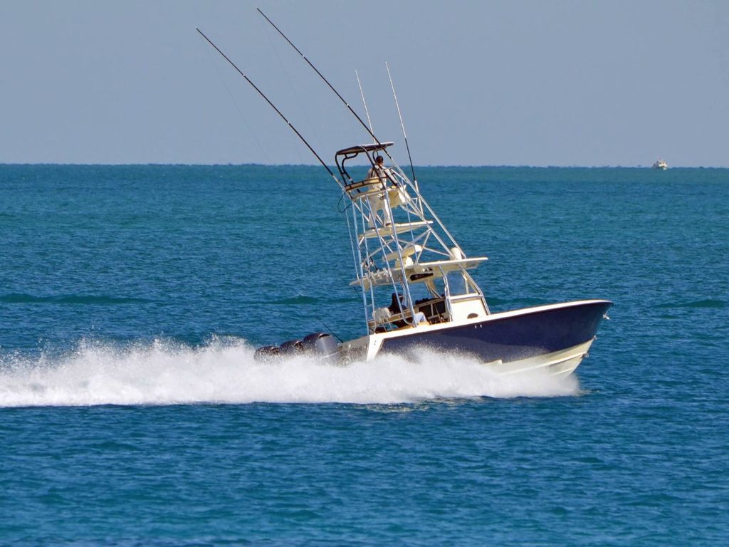 A sporfishing boat with a flybridge, speeding offshore near the Florida coast on a sunny day