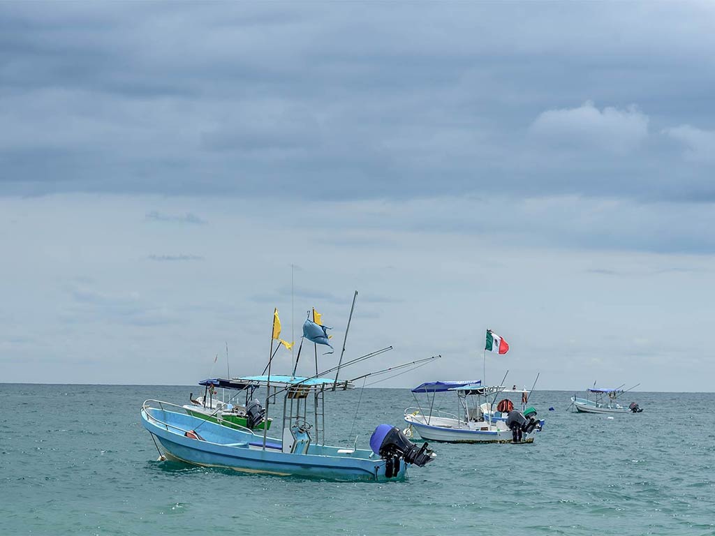 Four panga boats lie with flags docked in the nearshore waters out of Ensenada during a cloudy day