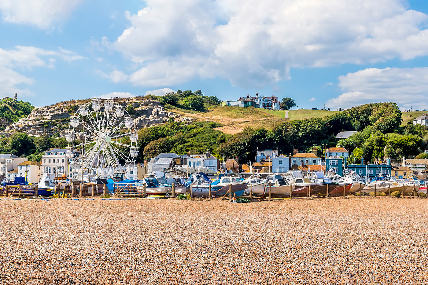 A view of Hastings Old Town from the beach, with fishing boats on the stones and cliffs in the distance