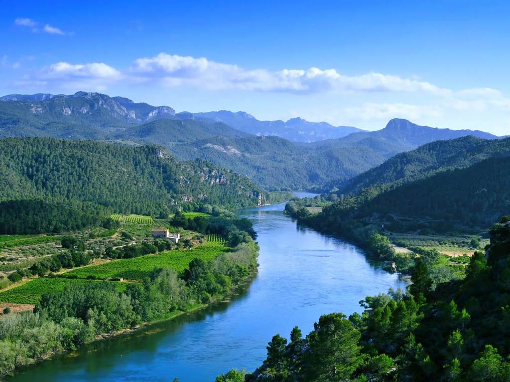 An aerial view of the Ebro River passing through greenery and mountains on a sunny day