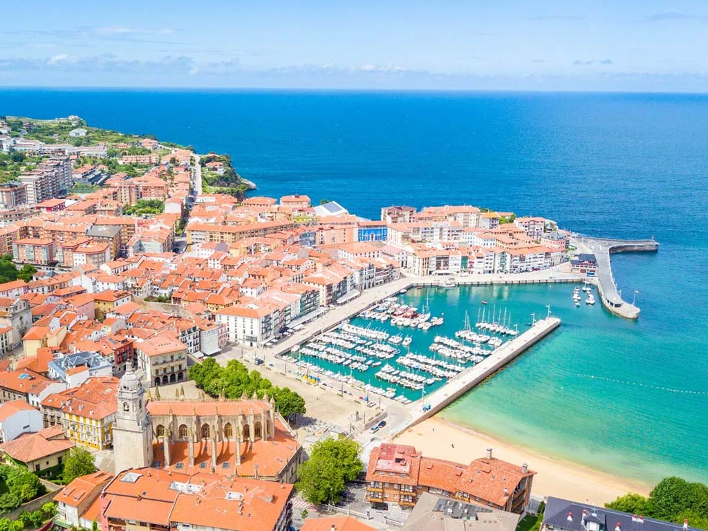 An aerial view of a fishing town on the Basque Coast, showing a port with charter boats docked, and the ocean