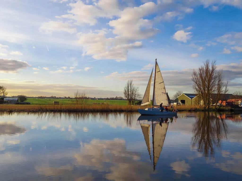 A photo featuring a sailboat standing still on the water on a canal in the Netherlands