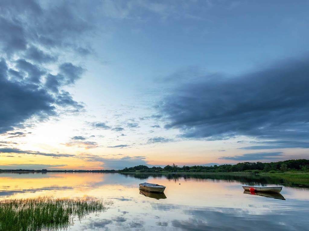 A photo of two fishing boats standing still out on Western Jutland's Skanderborg Lakes at sunset.