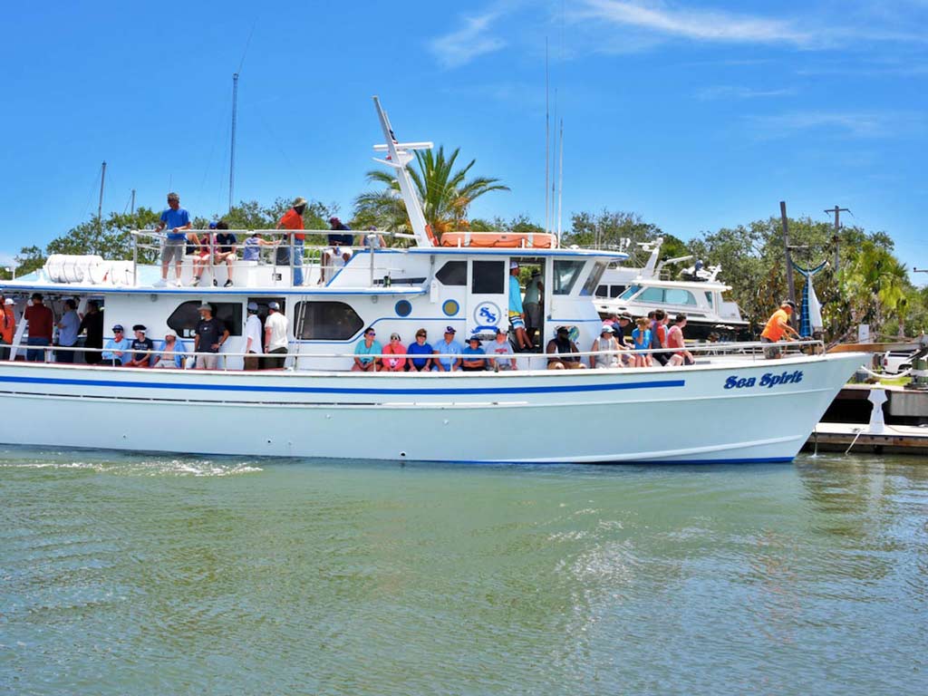 A party boat named "Sea Spirit" next to a dock with a large group of anglers sitting and standing on board getting ready to head out