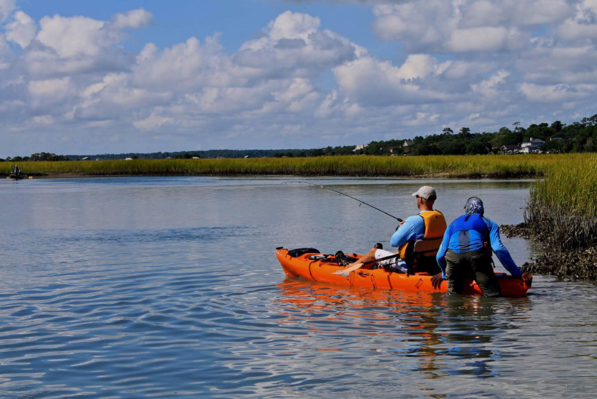 A kayak angler at a fishing therapy session being pushed out into calm water by a volunteer