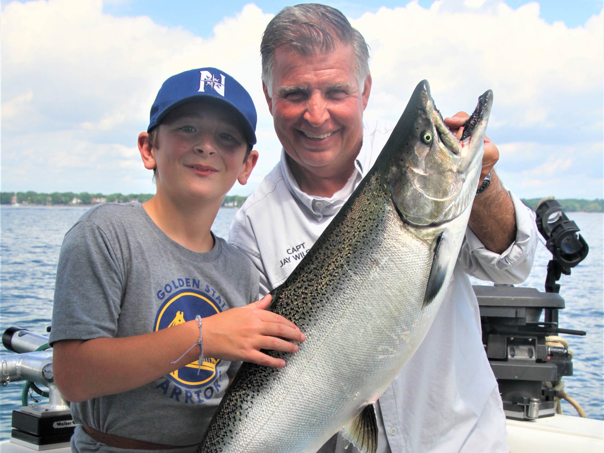 Grandfather and grandson holding a big Chinook Salmon with water and blue skies in the background