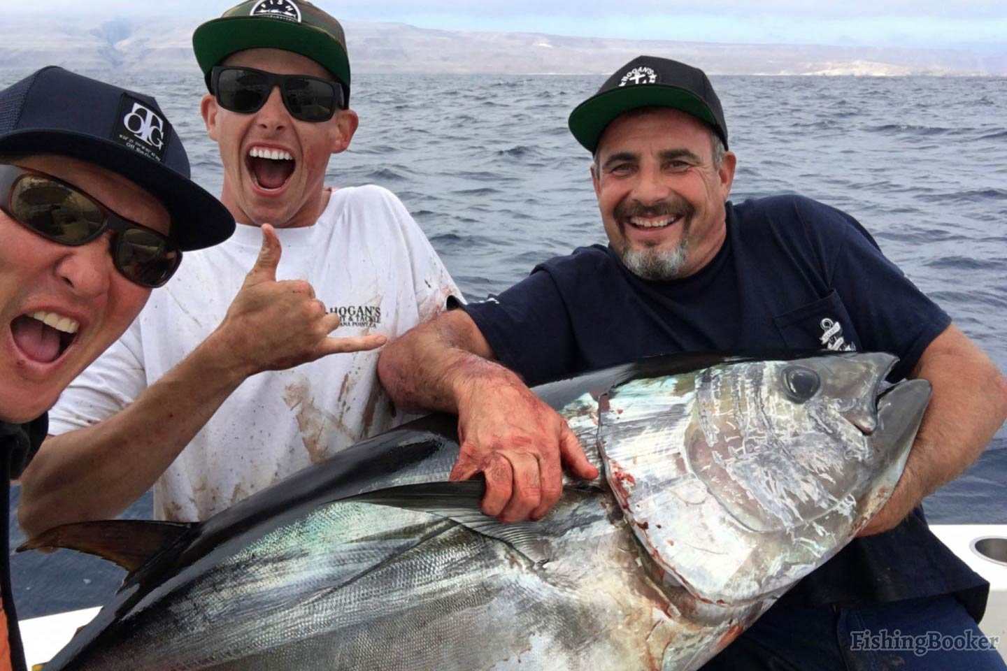 Three happy anglers in baseball caps showing off a large Bluefin Tuna caught in Los Angeles's waters while on a fishing boat.