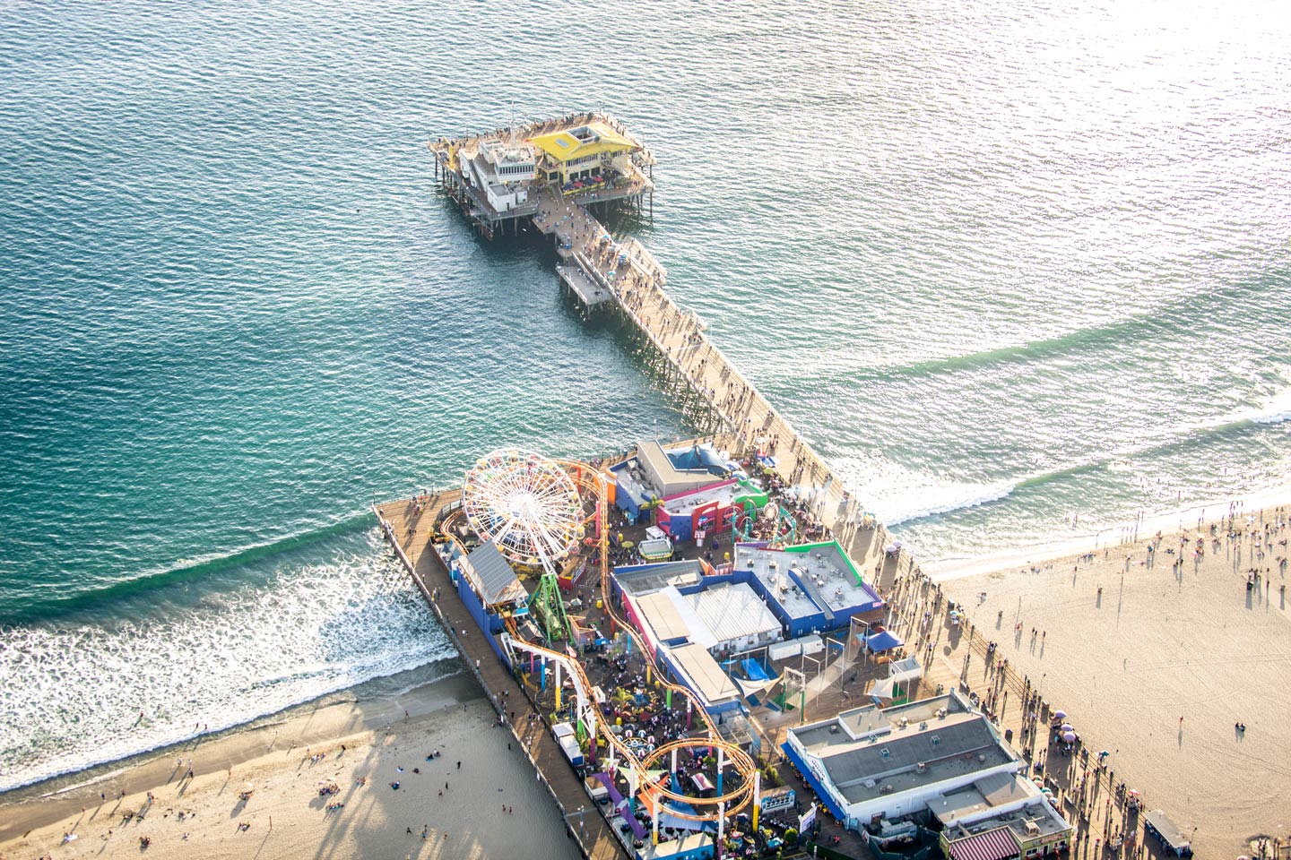 An aerial view of Los Angeles's Santa Monica Pier, with the pier stretching out into the Atlantic Ocean from the bottom, and a theme park on the left of it.