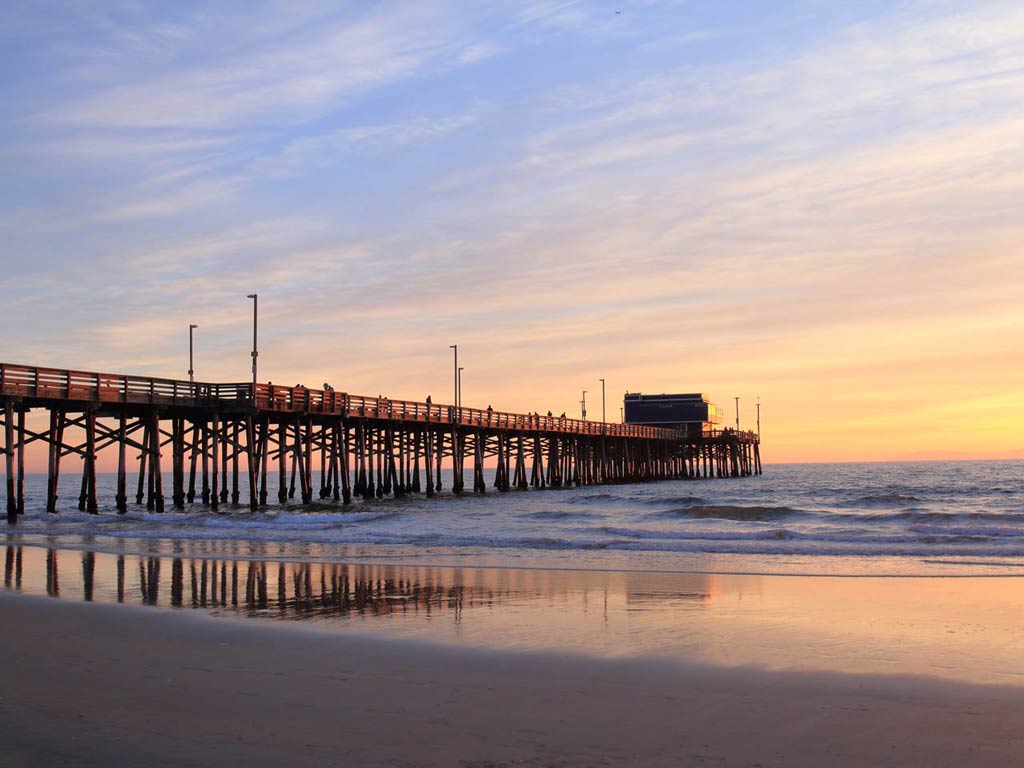 A photo of the famous landmark Newport Beach Pier taken at sunset during the calm seas and empty beach 