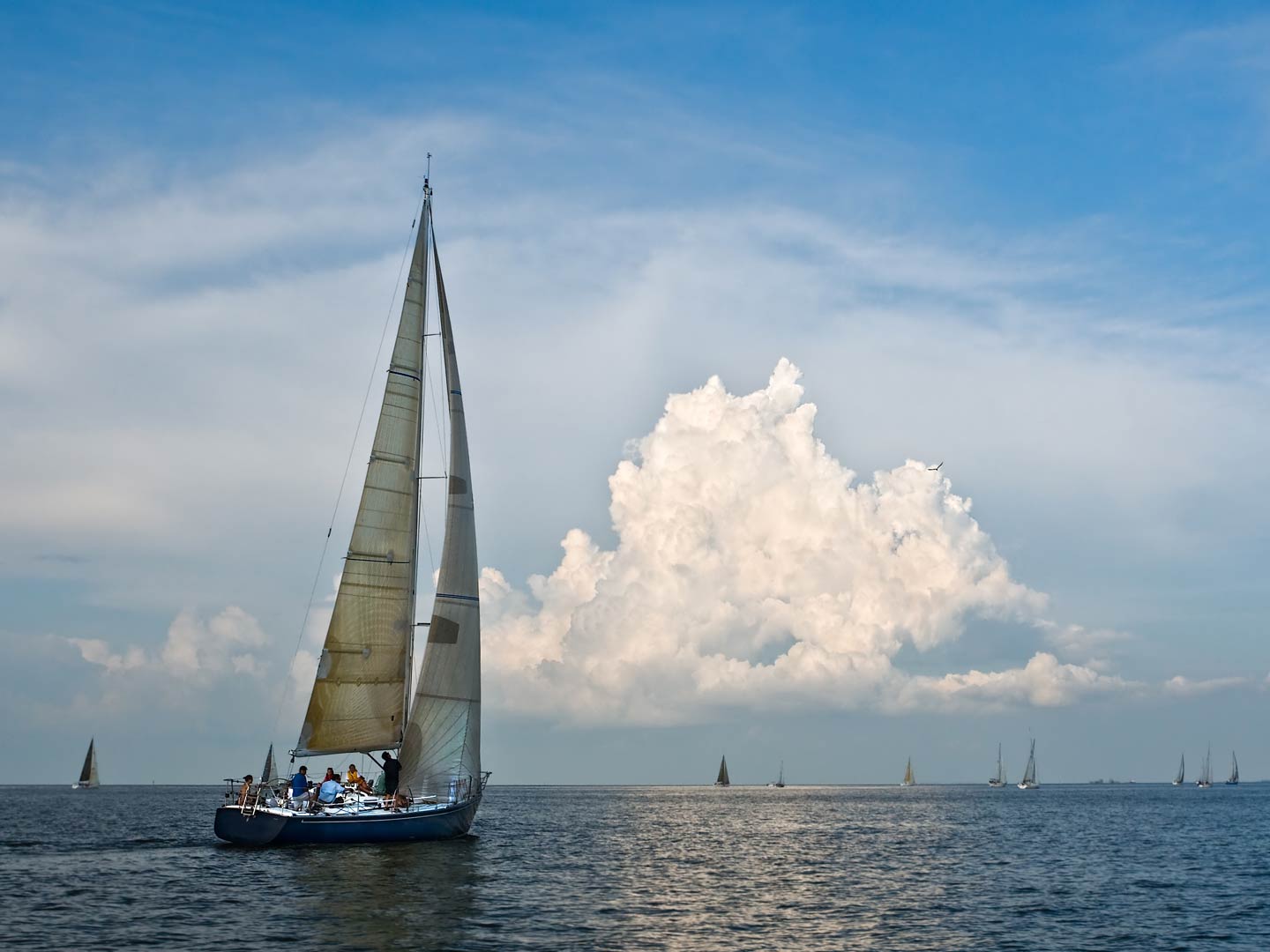 A sailboat on the waters of Galveston Bay, with numerous others in the distance on a day with sunny intervals