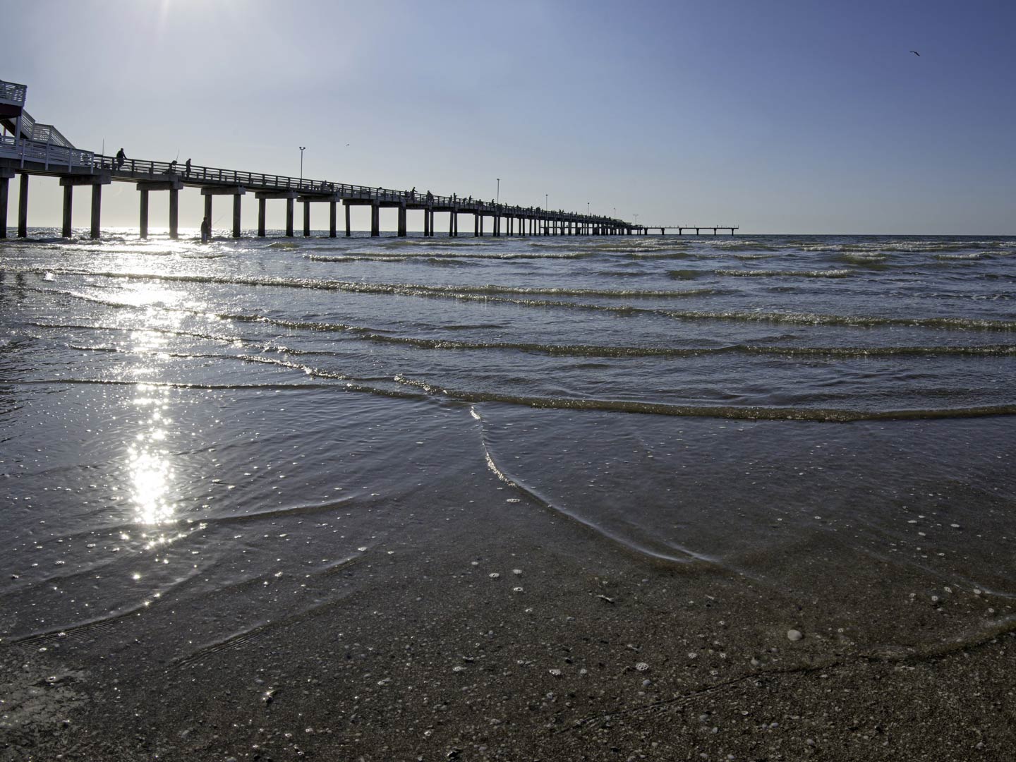 A view of a fishing pier in Galveston Bay, as seen from the beach on a sunny day