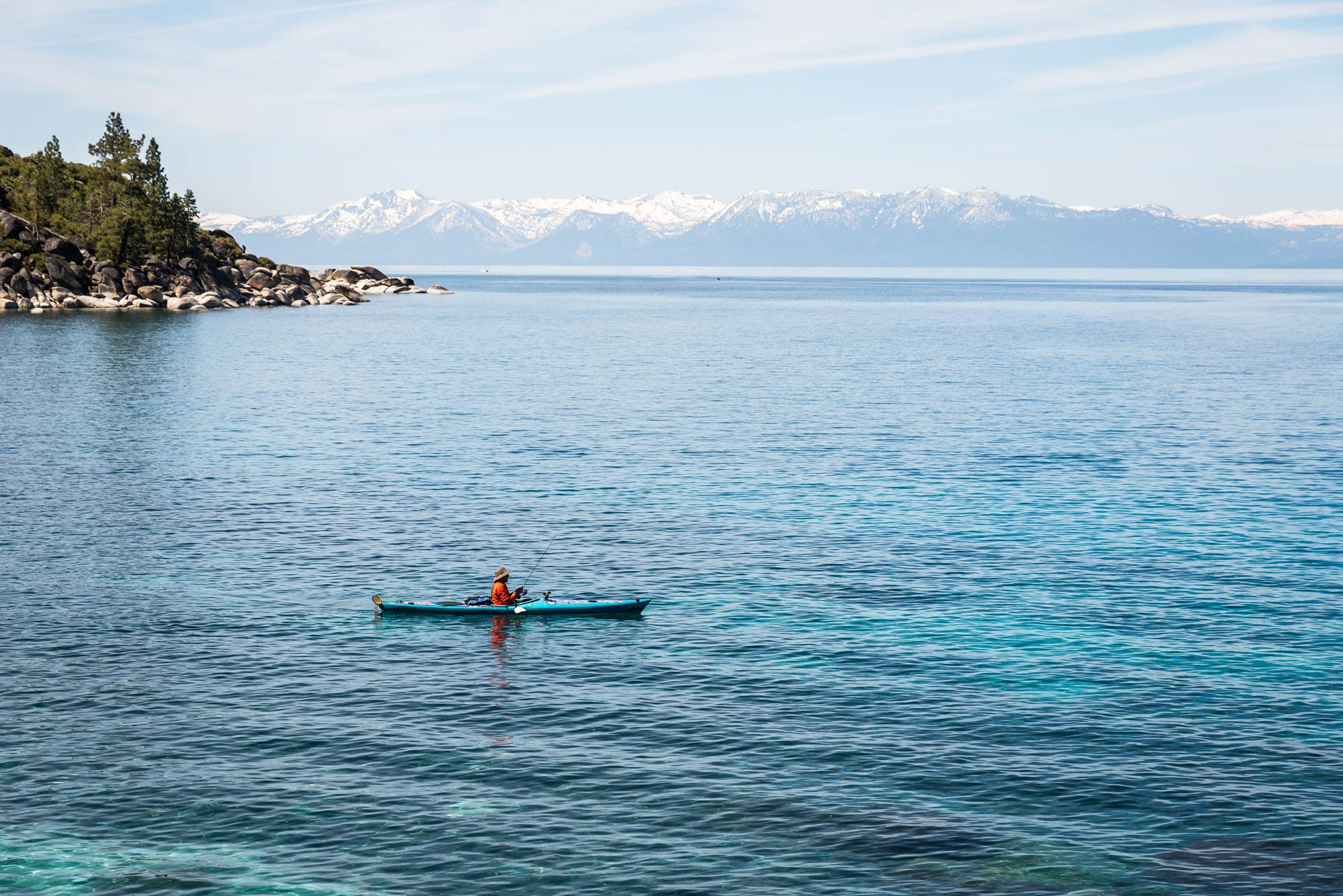A lone kayak fisherman on Lake Tahoe, with mountains in the background