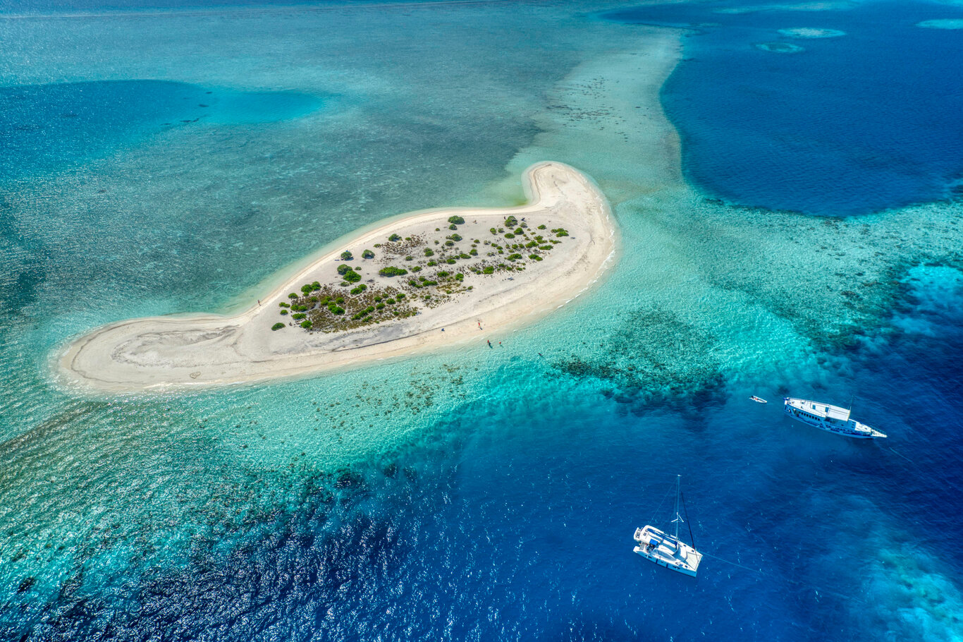 Ein Blick auf eine kleine Insel der Malediven mit Fischerbooten, die davor vor Anker liegen.