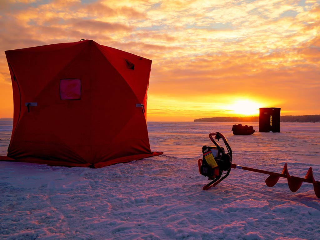 A tent and an ice drill on a frozen lake as seen during the sunset