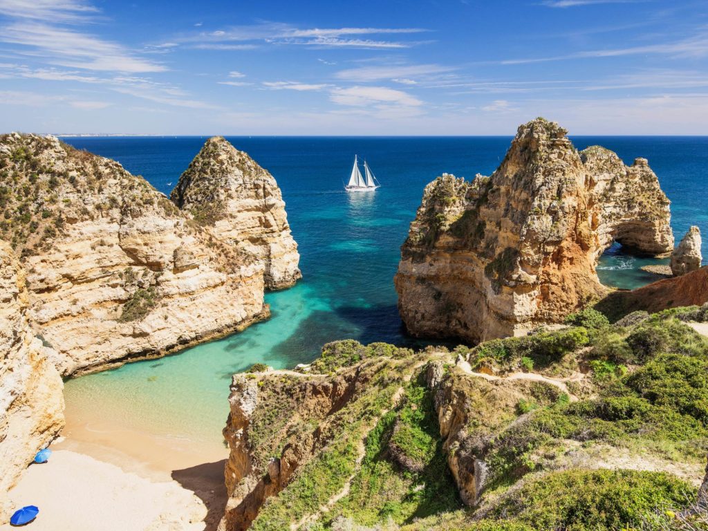 A small bay on the coast of Portugal, with a sailboat in the background.