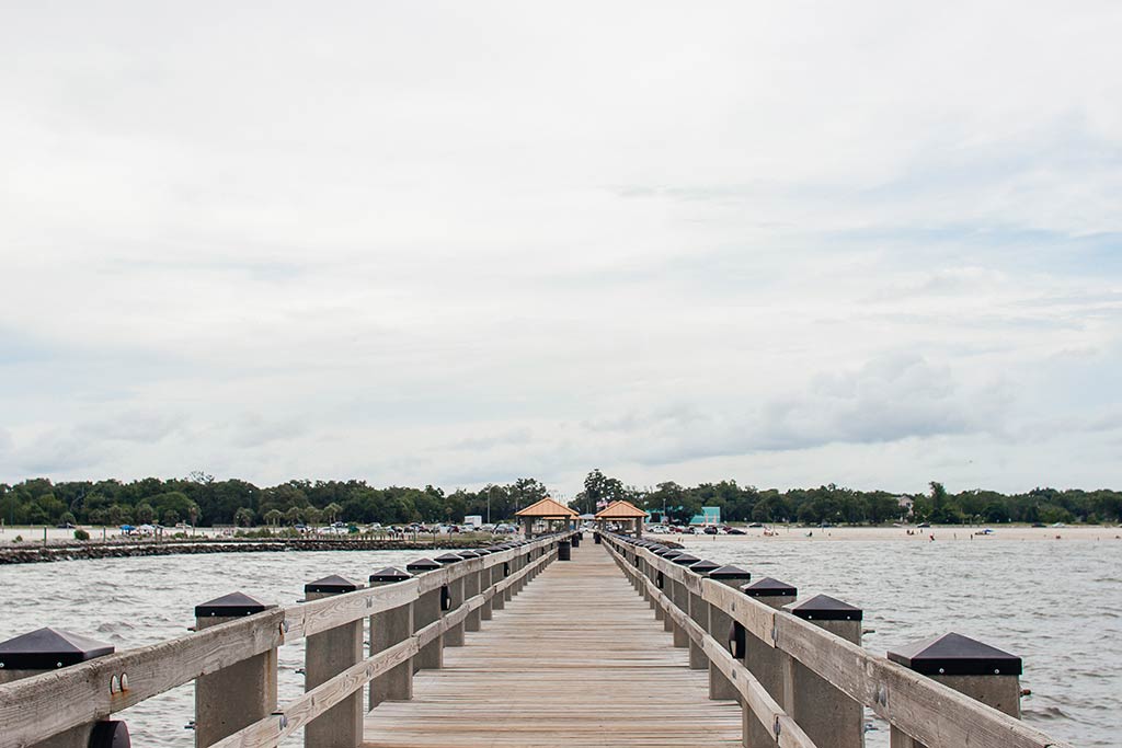 A view along a wooden fishing pier in Gulfport, Mississippi on a cloudy day with land visible across the water in the distance