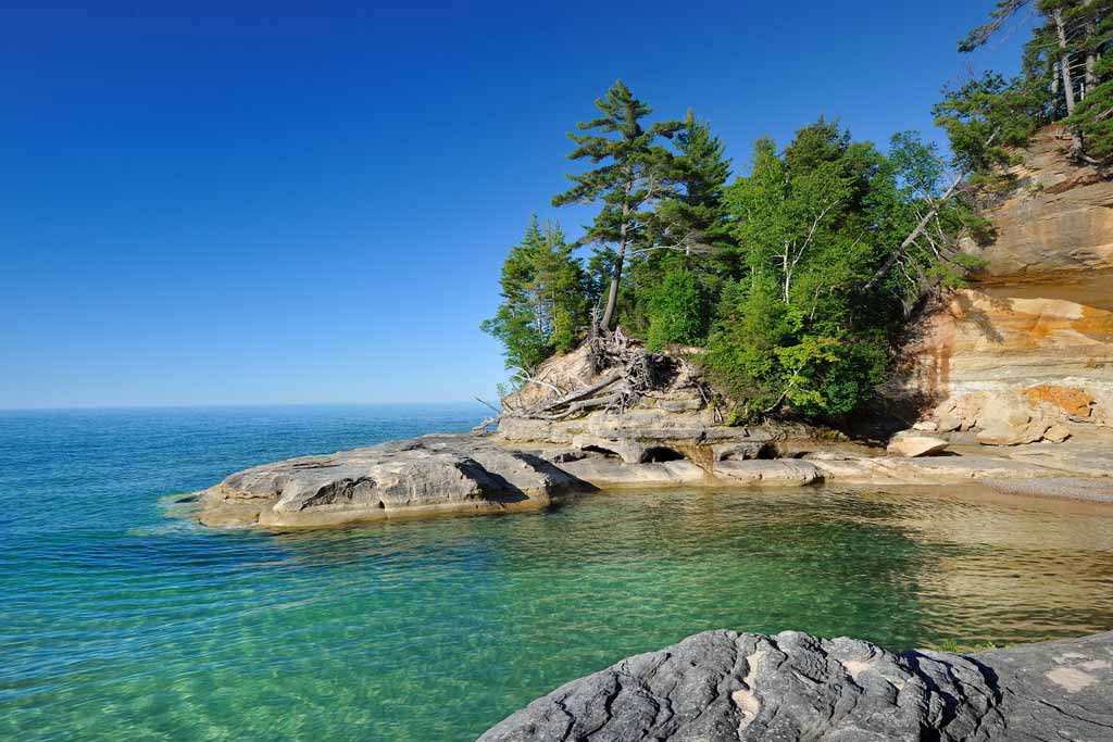 A photo showing rocky Lake Ontario shores with clear skies and beautiful, clear water.