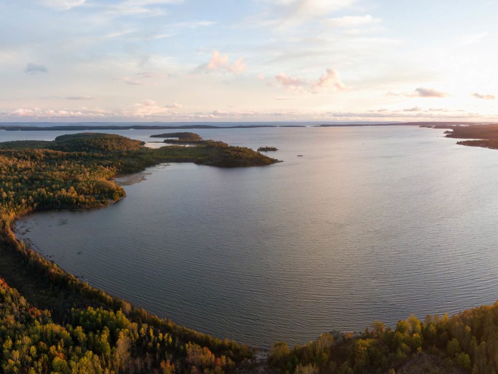 An aerial view of Lake Huron towards the end of the day, with a view of a bay in the foreground and the wide expanse of the lake in the distance