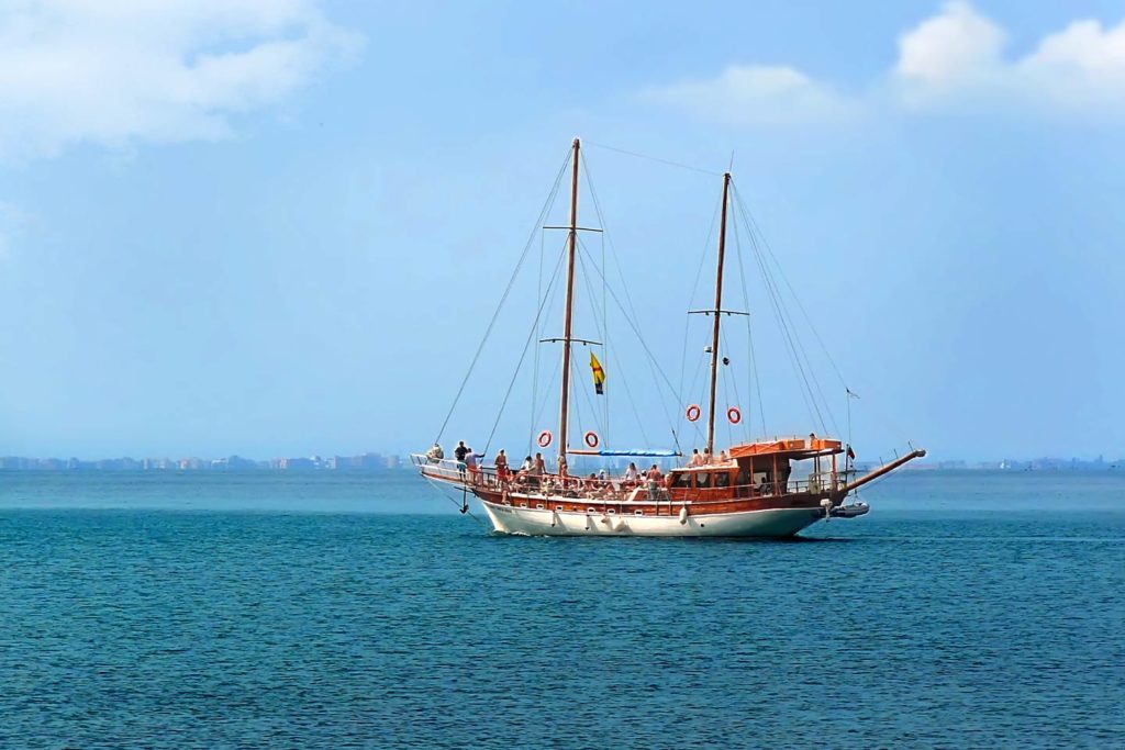 A party boat on the water, with two large masts sailing off to productive fishing grounds. 