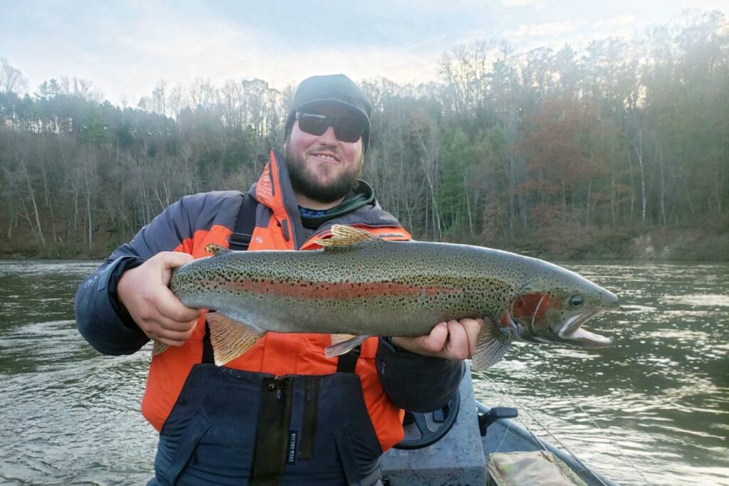 A man holds a Steelhead with the river behind him