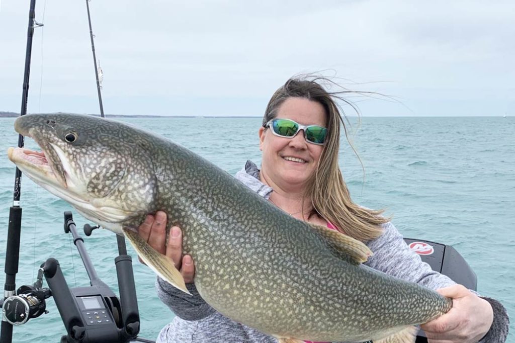 A lady holds a large Lake Trout aboard a Chicago fishing charter