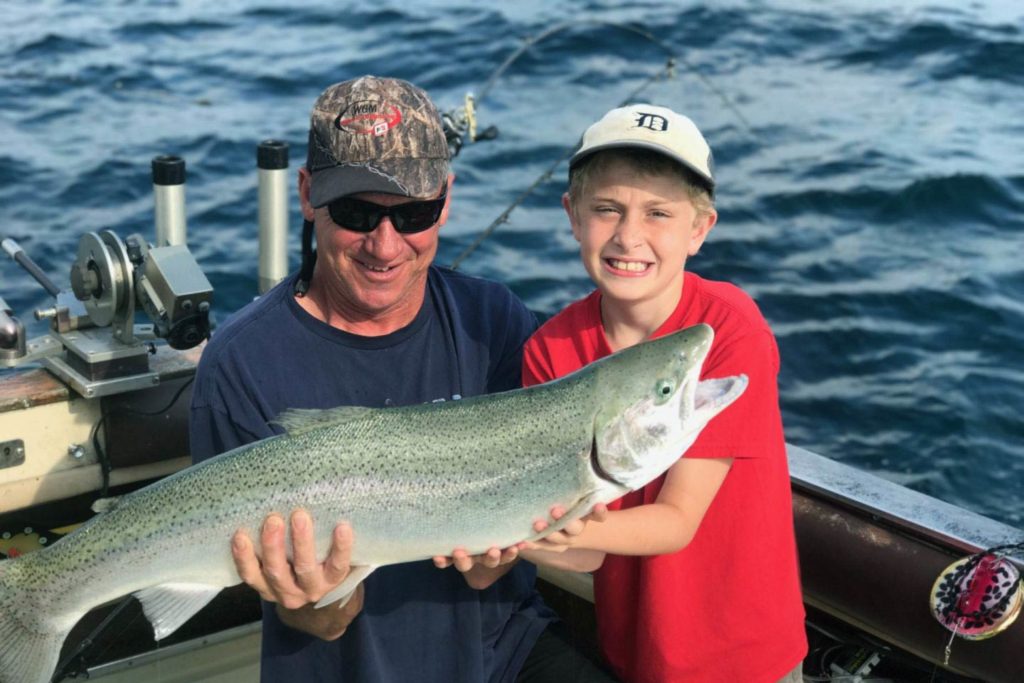 A man and a child hold a Steelhead aboard a boat