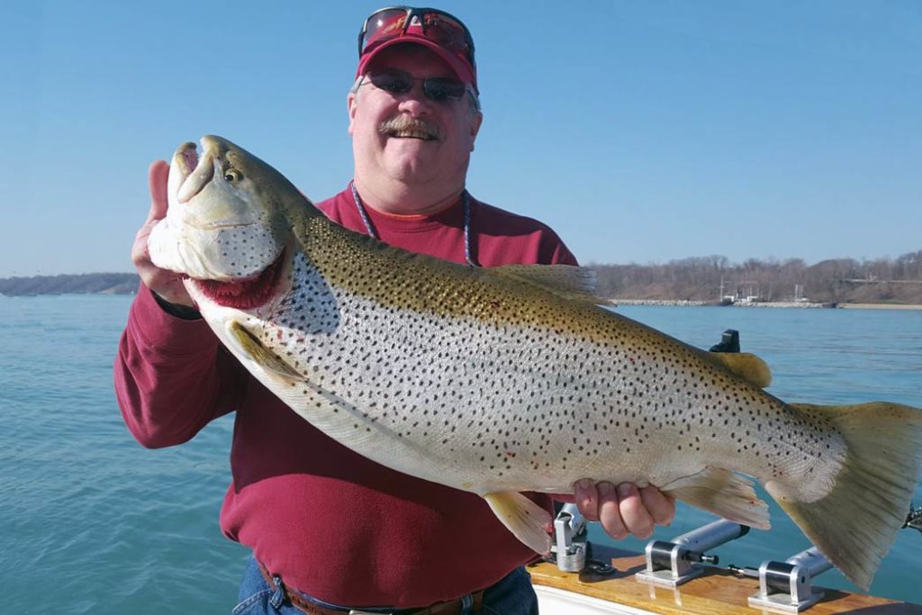 A happy man holds a Brown Trout on a charter boat with water behind him