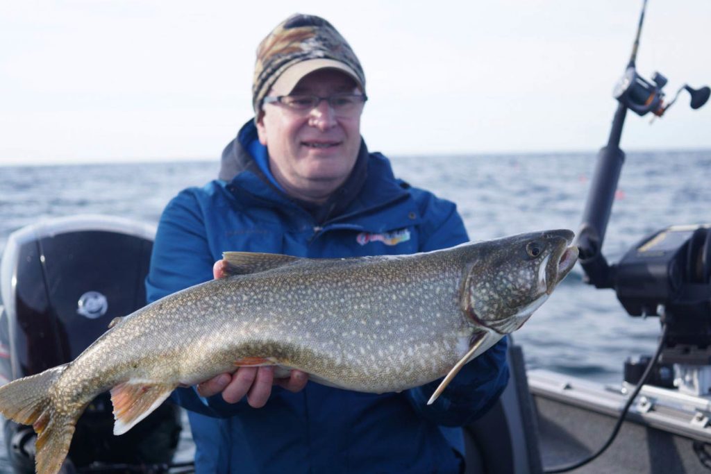 A man holds a large Lake Trout aboard a charter on Lake Michigan
