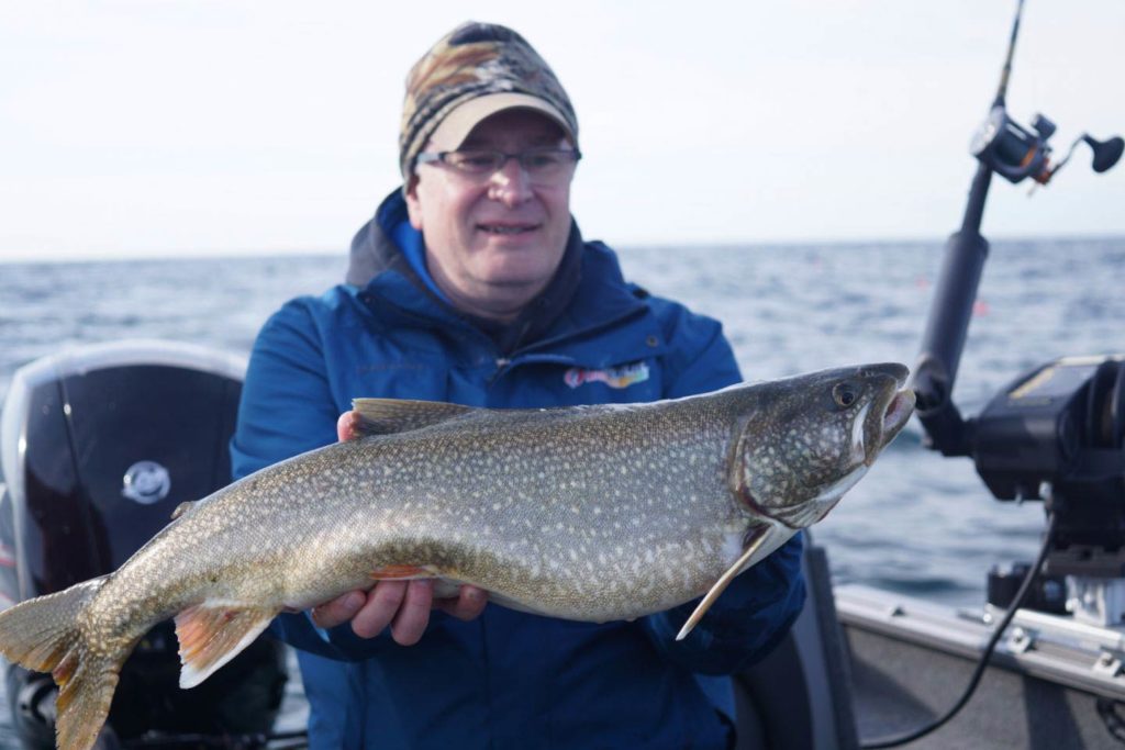 A man holds a large Lake Trout aboard a charter on Lake Michigan 