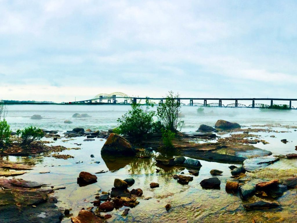 St. Marys River scenery with rocks, bushes, and a bridge in the background