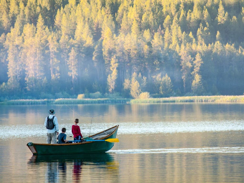 An adult male angler and two younger anglers sitting on a fishing boat and fishing in a lake or a river on a sunny day