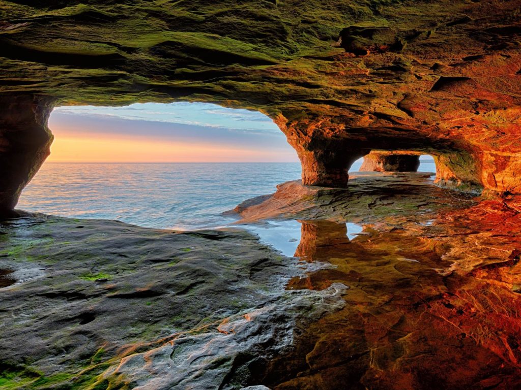 A view out to Lake Superior from within a cave, with the sunset forming a red light on the rock formations