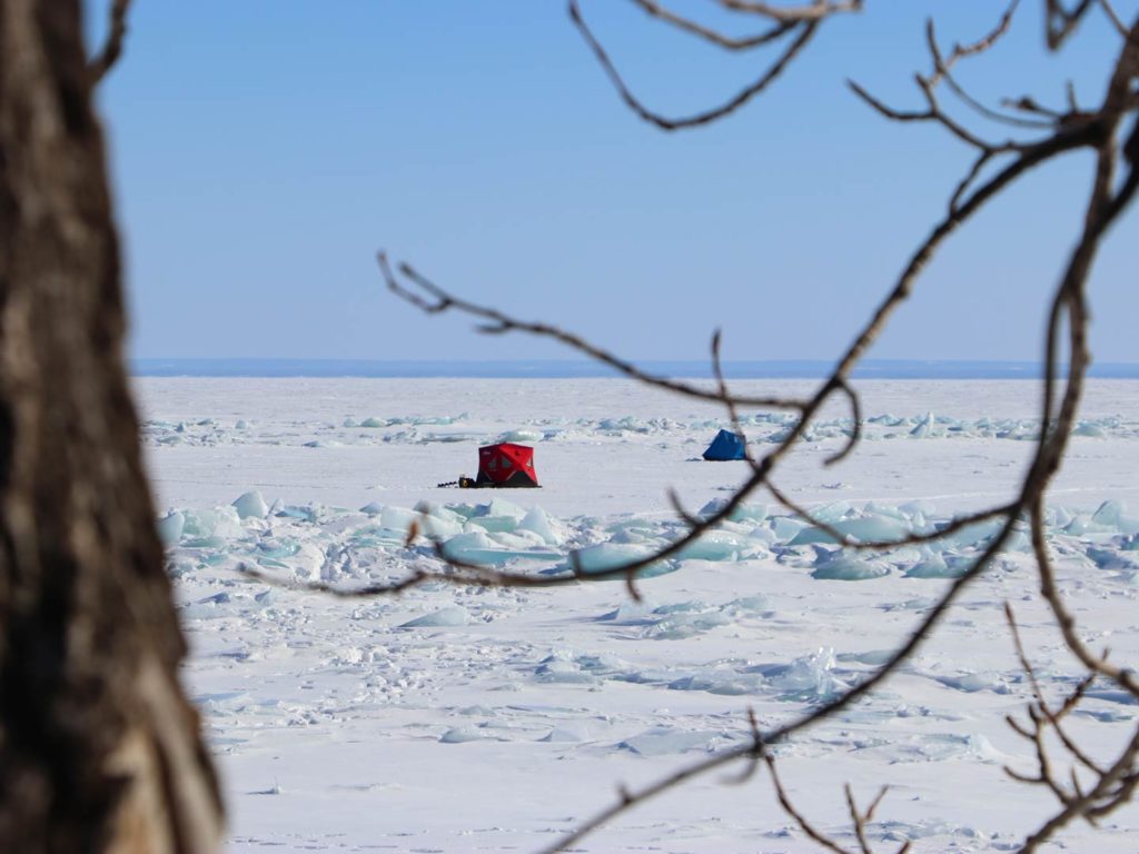 A voyeristic view through the woods of ice fishing tents on Lake Superior on a clear day in the winter