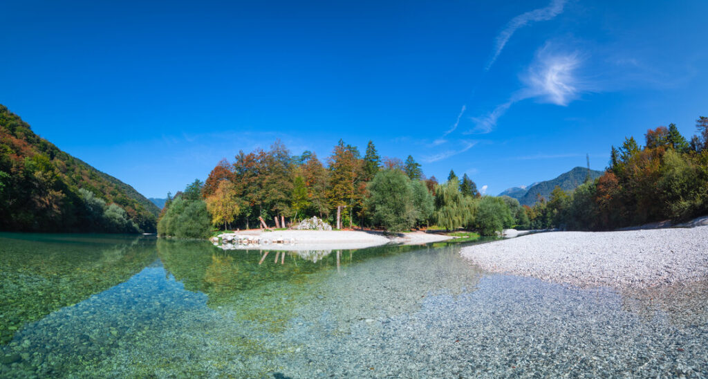 Der Zusammenfluss von Soča und Tolminka bei Tolmin in Slovenien. Es gibt einen wei&szlig;en Kiesstrand auf der rechten Seite und Wald im Hintergrund.
