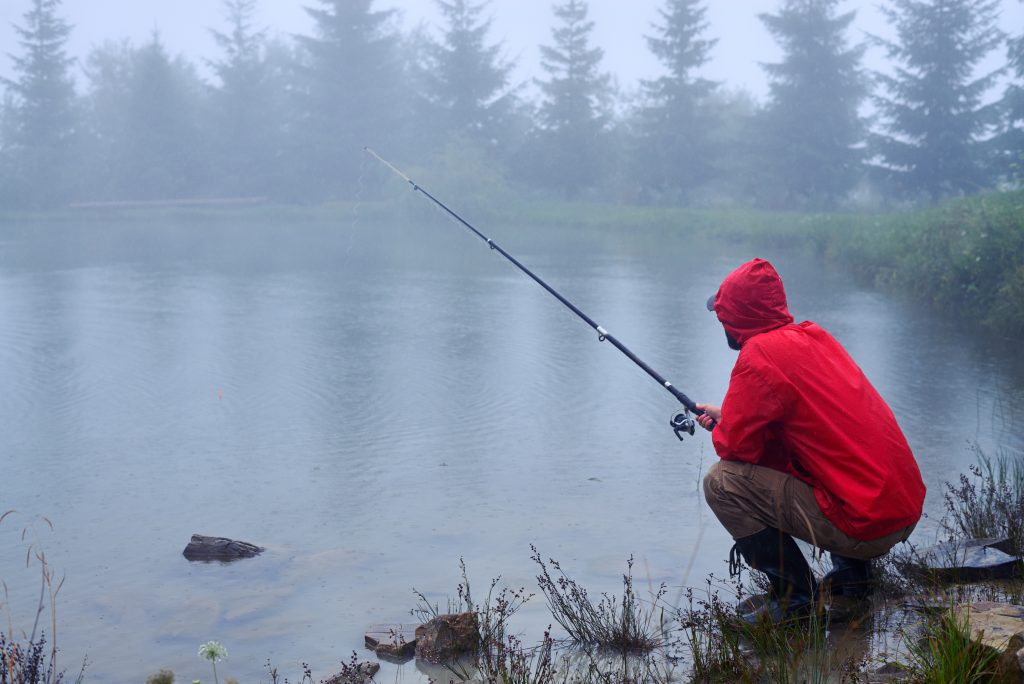 Angler, der bei schlechtem Wetter an einem Teich angelt.