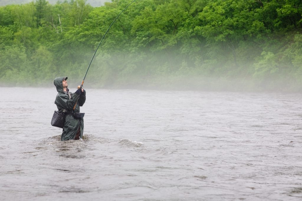 Ein Angler steht bei Regen in einem Fluss und angelt.