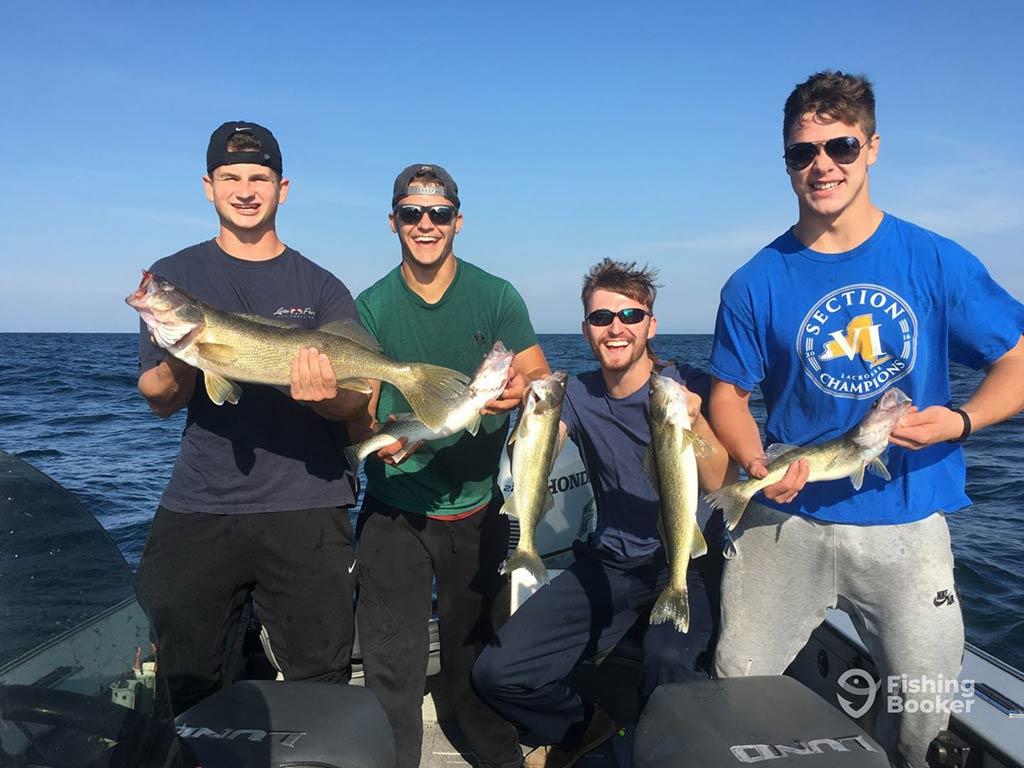 Four people are on a boat on the Niagara River, proudly holding several Walleye fish and smiling at the camera, with a clear blue sky in the background.