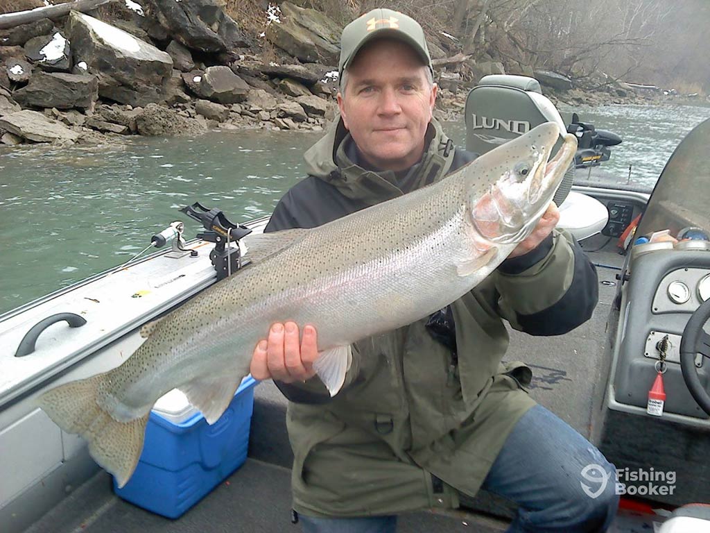A person holding a large Steelhead fish while sitting in a boat on the Niagara River, showcasing a successful day of fishing.