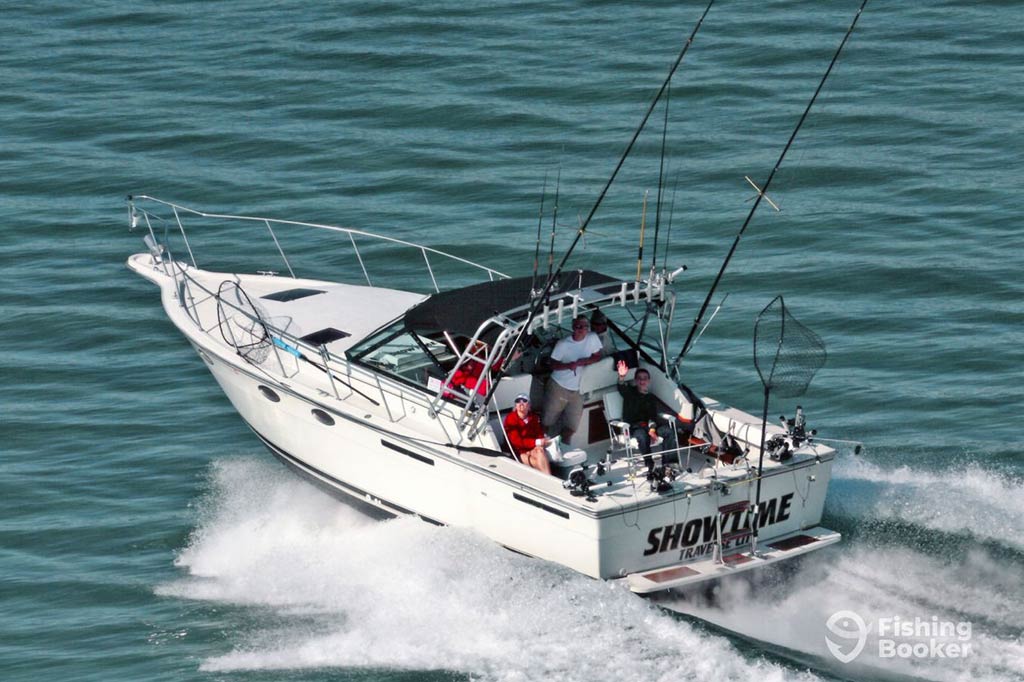 An aerial view of a fishing charter speeding off along a lake near Traverse City, with anglers visible on the deck looking up towards the camera