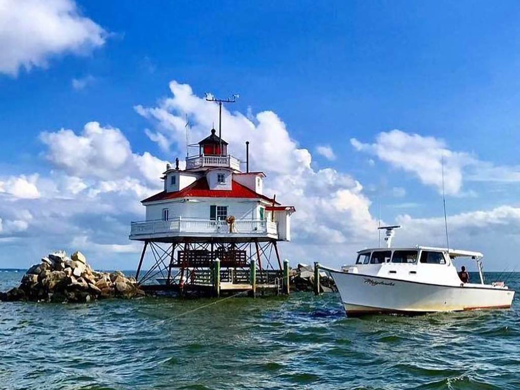 A photo of a charter fishing boat anchored next to a lighthouse in the Chesapeake Bay during a bright day