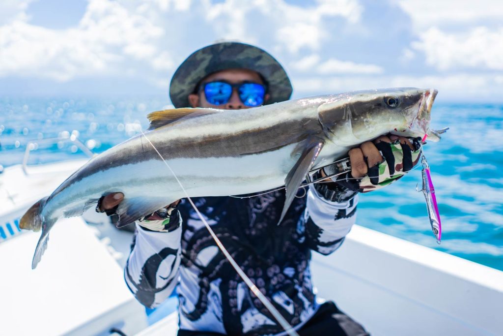 An angler holding out a Cobia aboard a charter boat