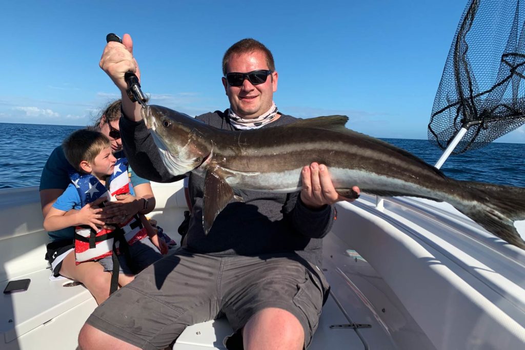 A picture showing a female angler with a young child and a male angler holding a freshly caught Cobia while on a charter fishing boat in Florida