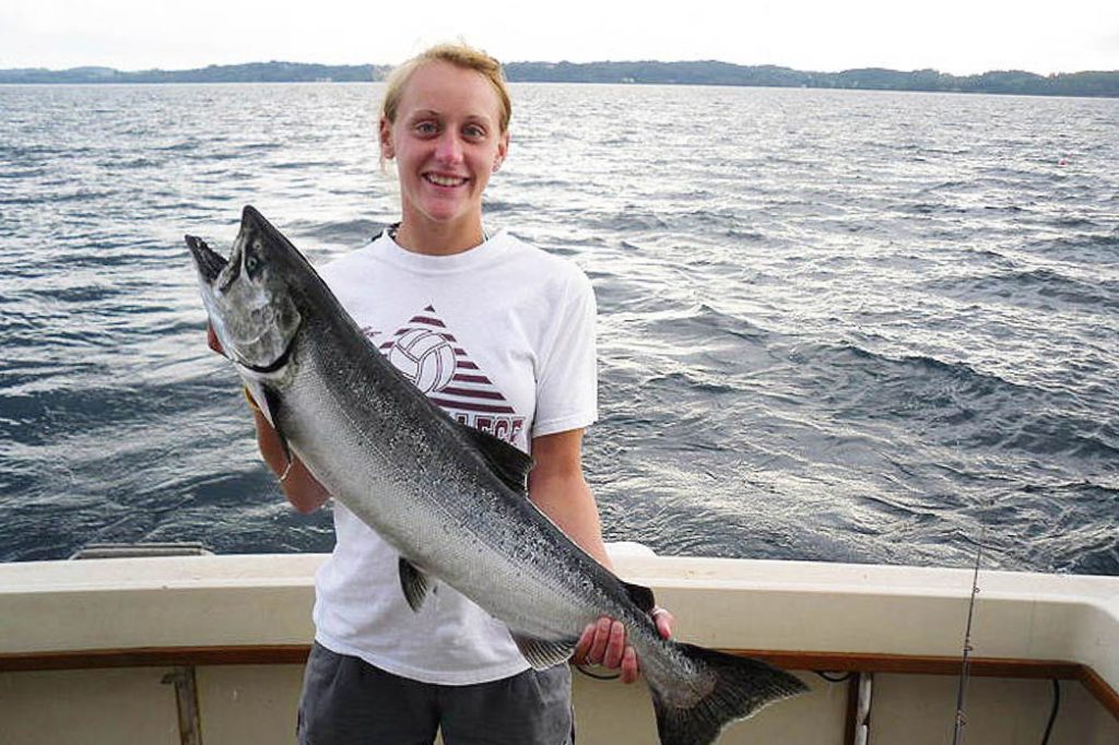 A woman holds a Chinook Salmon aboard a charter boat in Traverse City with the water behind her