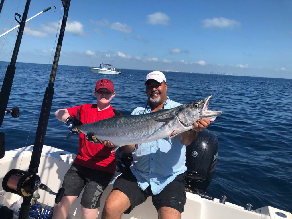 A man and a child sitting on a boat, holding a King Mackerel