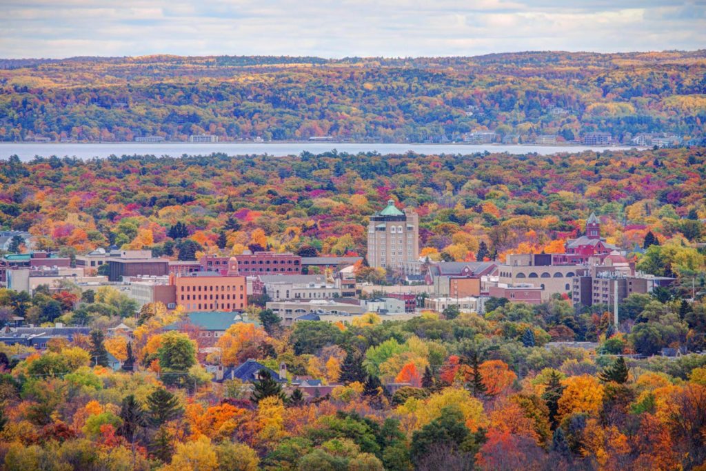 A view of Traverse City's skyline with lots of forestry in fall in the foreground and waters in the background