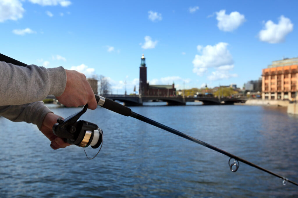Ein Angler h&auml;lt eine Spinnrute, vor der Kulisse der Stockholmer Innenstadt.